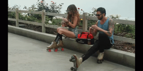 A Woman Wearing Roller Skates Sits Next To A Man GIF