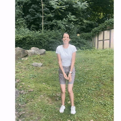 A Woman Wearing Shorts And A White Shirt Stands In A Grassy Field GIF
