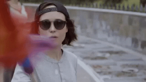 A Woman Wearing Sunglasses And A Baseball Cap Is Standing Next To A Skateboard . GIF