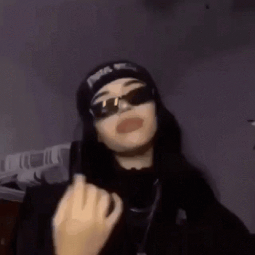 A Woman Wearing Sunglasses And A Beanie Is Giving A Middle Finger . GIF