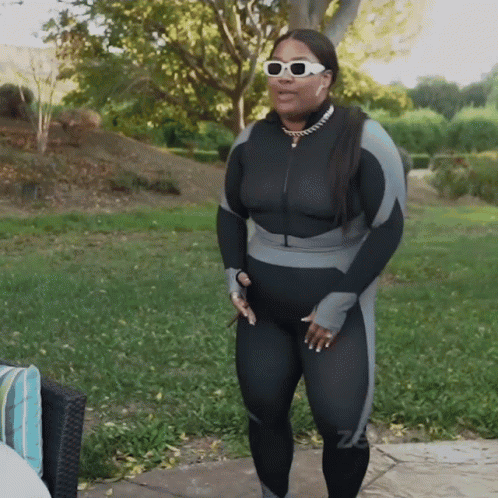 A Woman Wearing Sunglasses And A Black And Grey Jumpsuit GIF