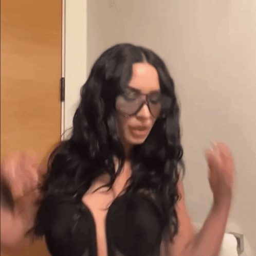 A Woman Wearing Sunglasses And A Black Bra Is Standing In A Bathroom . GIF