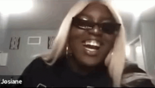 A Woman Wearing Sunglasses And A Black Shirt Is Smiling While Looking At The Camera . GIF