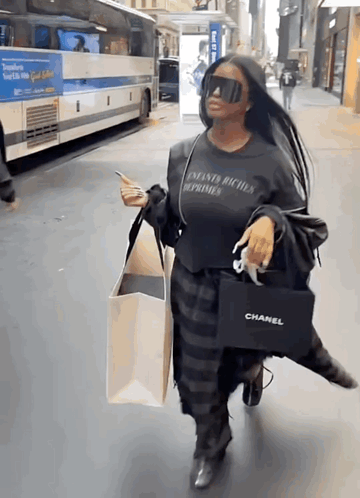 A Woman Wearing Sunglasses And A Chanel Bag Walks Down A Street GIF
