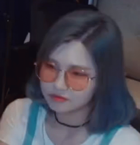 A Woman Wearing Sunglasses And A Choker Is Sitting On A Couch . GIF