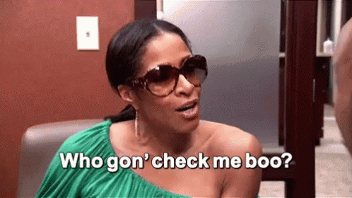 A Woman Wearing Sunglasses And A Green Dress Is Sitting In A Chair And Talking To Another Woman . GIF