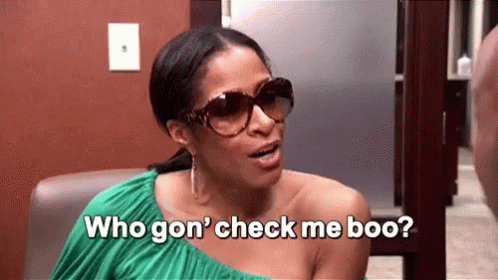 A Woman Wearing Sunglasses And A Green Dress Is Sitting In A Chair And Talking To Another Woman . GIF
