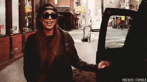A Woman Wearing Sunglasses And A Hat Is Getting Out Of A Car On A City Street . GIF