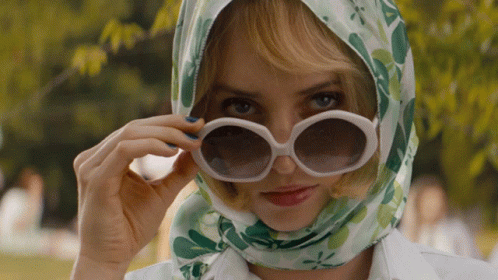 A Woman Wearing Sunglasses And A Head Scarf Looks At The Camera GIF