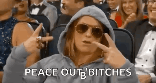 A Woman Wearing Sunglasses And A Hooded Jacket Is Sitting In A Crowd Of People . GIF
