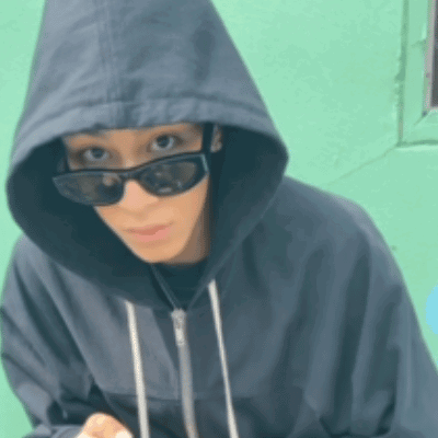 A Woman Wearing Sunglasses And A Hoodie Is Looking At The Camera GIF