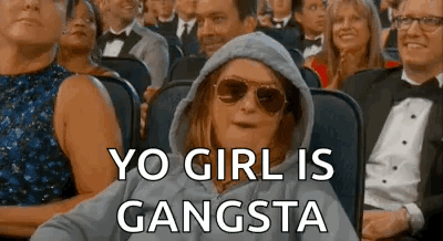 A Woman Wearing Sunglasses And A Hoodie Is Sitting In A Crowd Of People And Says `` Yo Girl Is Gangsta '' . GIF