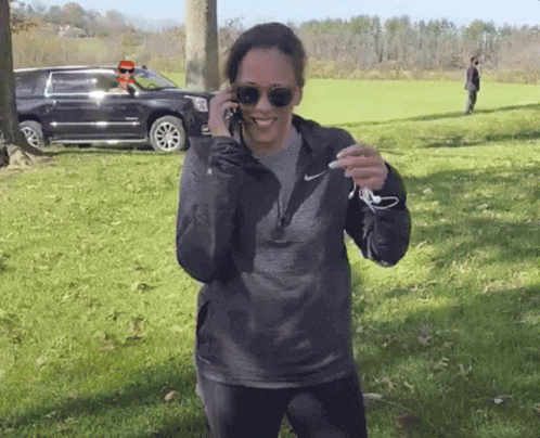 A Woman Wearing Sunglasses And A Nike Sweatshirt Talks On A Cell Phone GIF