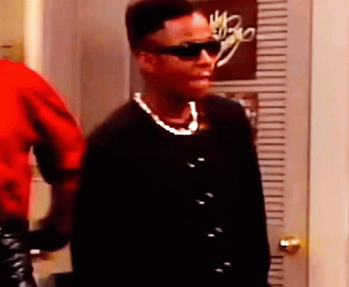 A Woman Wearing Sunglasses And A Pearl Necklace Is Standing Next To A Door . GIF