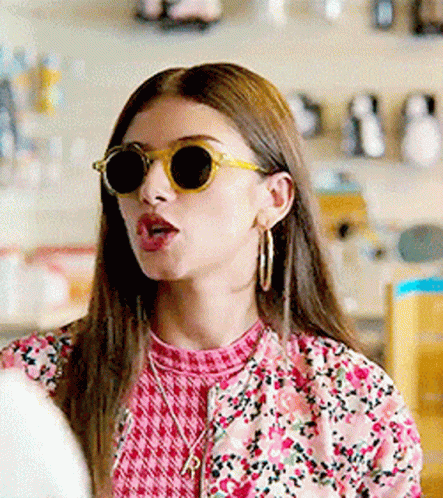 A Woman Wearing Sunglasses And A Pink Floral Jacket Is Making A Funny Face . GIF