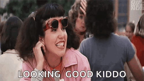 A Woman Wearing Sunglasses And A Pink Jacket Is Sitting In A Crowd Of People And Talking On A Cell Phone . GIF