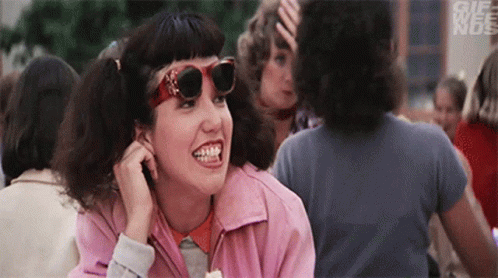 A Woman Wearing Sunglasses And A Pink Jacket Is Smiling In A Crowd . GIF