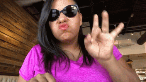 A Woman Wearing Sunglasses And A Pink Shirt Making A Face GIF