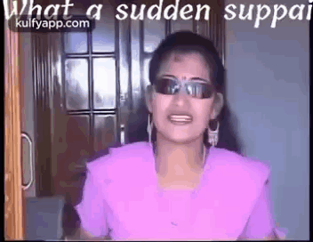 A Woman Wearing Sunglasses And A Purple Shirt Is Standing In Front Of A Door And Talking . GIF