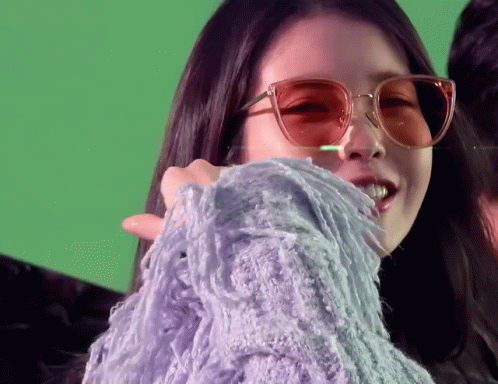 a woman wearing sunglasses and a purple sweater on a green background