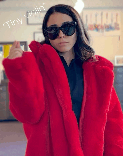 A Woman Wearing Sunglasses And A Red Fur Coat With The Words " Tiny Violin " Below Her GIF