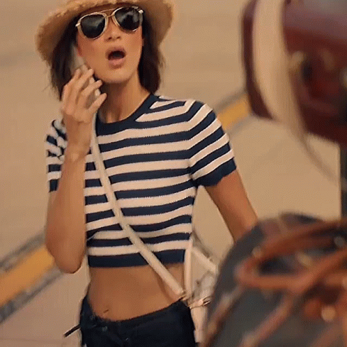 A Woman Wearing Sunglasses And A Striped Shirt Is Talking On A Cell Phone GIF