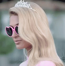 A Woman Wearing Sunglasses And A Tiara Is Wearing A Pink Dress And A Pink Top . GIF