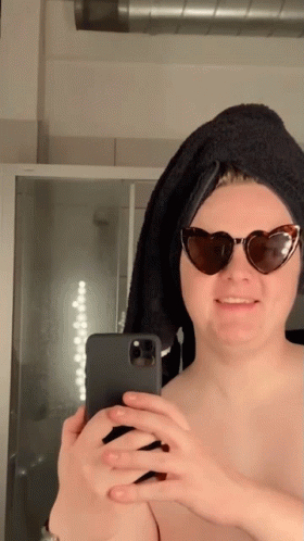 A Woman Wearing Sunglasses And A Towel On Her Head Takes A Selfie With Her Phone GIF