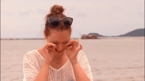 A Woman Wearing Sunglasses And A White Lace Shirt Looks Down GIF