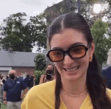 a woman wearing sunglasses and a yellow shirt is smiling and looking at the camera .