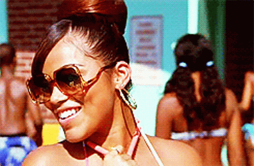 A Woman Wearing Sunglasses And Earrings Is Smiling GIF