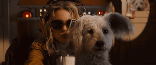 A Woman Wearing Sunglasses And Headphones Holds A Small White Dog GIF