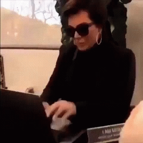 A Woman Wearing Sunglasses And Hoop Earrings Is Typing On A Laptop Computer . GIF