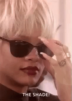 A Woman Wearing Sunglasses And Red Lipstick Is Looking Down At Something . GIF
