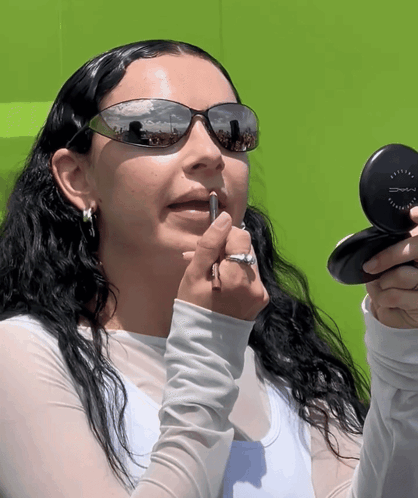 A Woman Wearing Sunglasses Applying Lipstick With A Mac Compact GIF