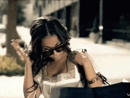 A Woman Wearing Sunglasses Is Holding A Bag And Looking At Something GIF