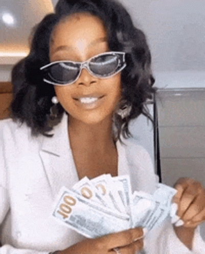 A Woman Wearing Sunglasses Is Holding A Fan Of Money In Her Hands . GIF