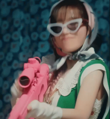 A Woman Wearing Sunglasses Is Holding A Pink Toy Gun . GIF