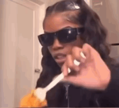 A Woman Wearing Sunglasses Is Holding A Spoon In Her Hand And Making A Funny Face . GIF