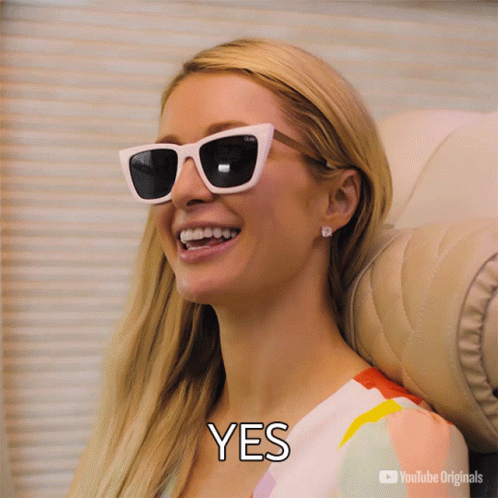 A Woman Wearing Sunglasses Is Smiling With The Word Yes Below Her GIF