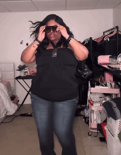 A Woman Wearing Sunglasses Is Standing In A Room With A Pink Cart GIF