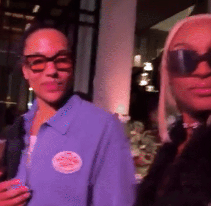 A Woman Wearing Sunglasses Is Standing Next To A Man Wearing A Purple Shirt . GIF