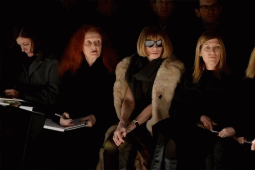 A Woman Wearing Sunglasses Sits In A Dark Room GIF