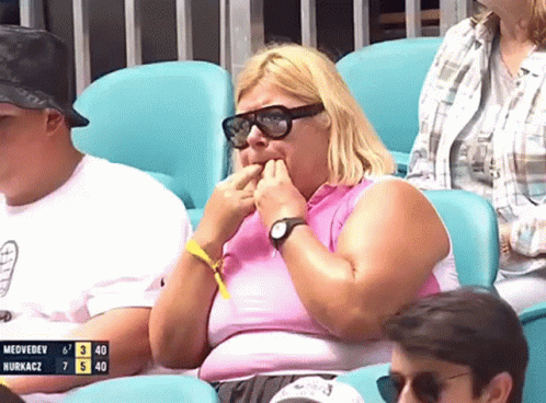 A Woman Wearing Sunglasses Sits In A Stadium Watching A Game Between Medvedev And Nurkacz GIF