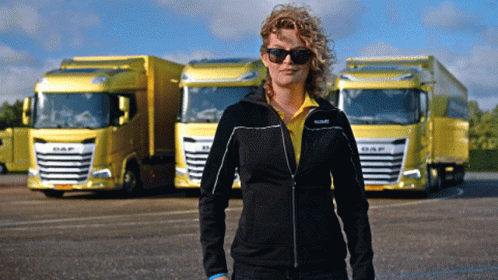 A Woman Wearing Sunglasses Stands In Front Of Yellow Daf Trucks GIF