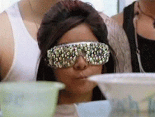A Woman Wearing Sunglasses With Rhinestones On Them Is Sitting At A Table GIF