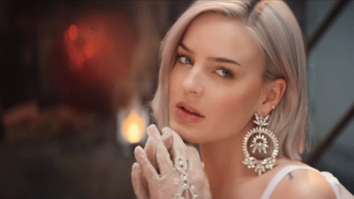 A Woman Wearing White Gloves And Large Earrings GIF