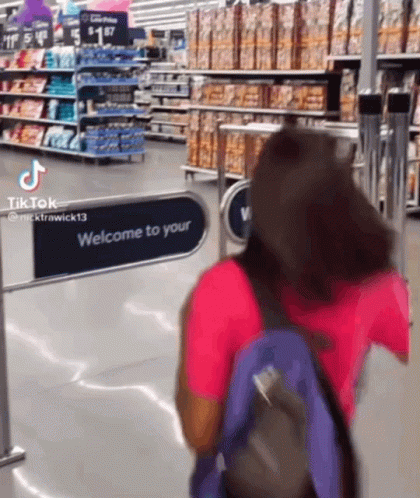 A Woman With A Backpack Is Walking Through A Welcome To Your Sign In A Grocery Store GIF