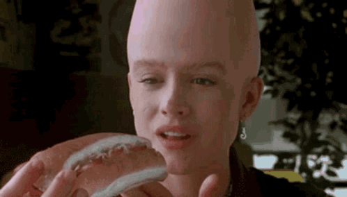 A Woman With A Bald Head Is Holding A Hot Dog . GIF
