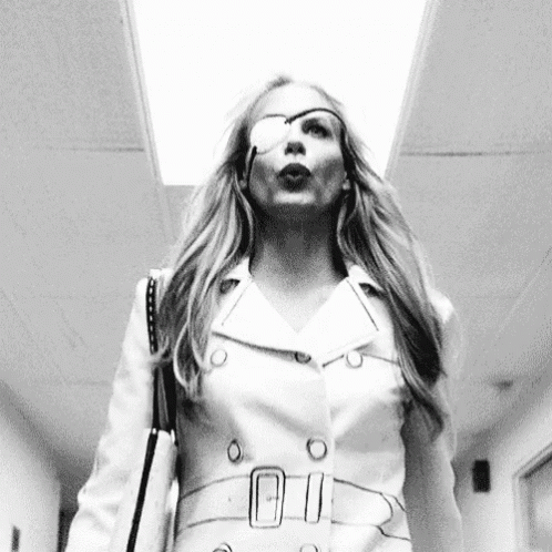 A Woman With A Bandage On Her Eye Is Walking Down A Hallway With A Purse . GIF